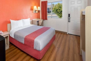 Habitació d'hotel amb llit, taules de nit, làmpada, finestra amb cortines i porta.