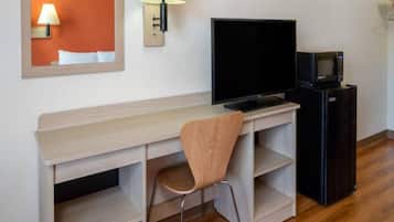 A hotel room with a wooden desk, a television, a microwave, and a chair.