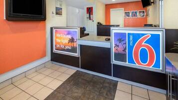 A motel reception desk with a digital screen displaying a message, a large number '6' sign, and a tiled floor.