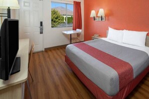 Habitació d'hotel amb llit, escriptori amb làmpada, cadira, taula petita i finestra amb vistes.