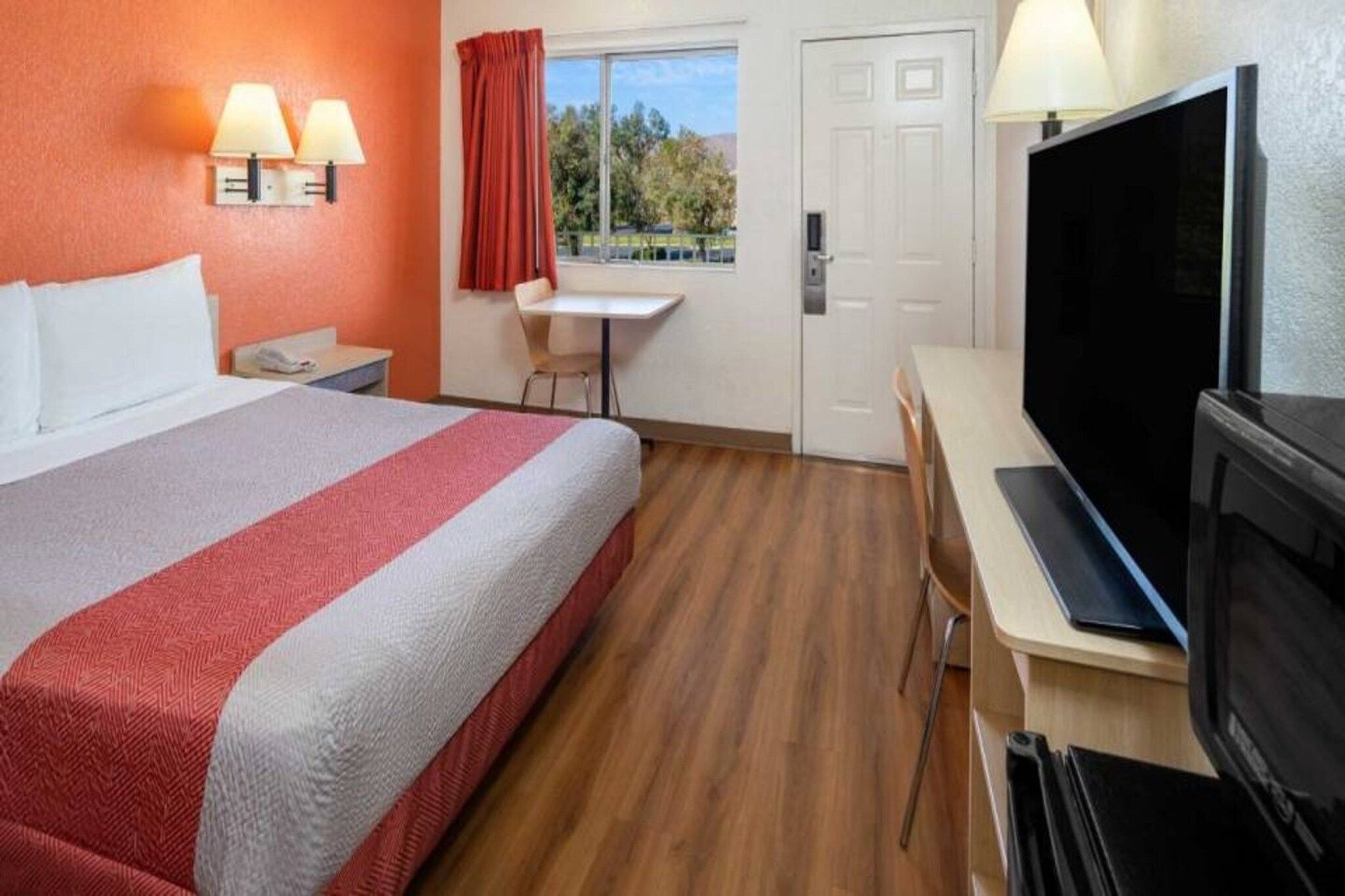 Ein Hotelzimmer mit Bett, Schreibtisch, Fernseher und einem Fenster mit Vorhängen.