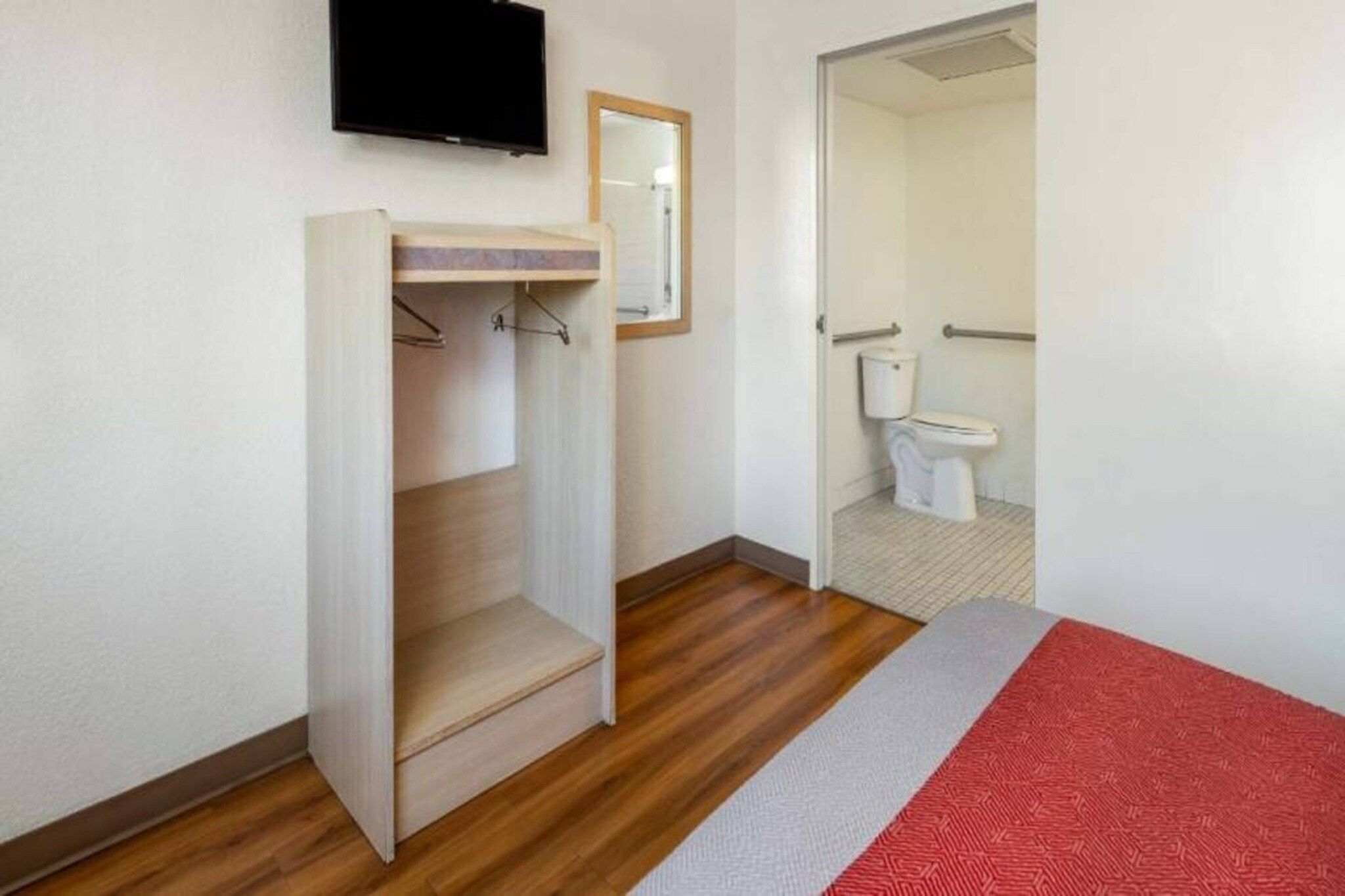 Une chambre à coucher avec un lit, un plancher en bois, une armoire, un miroir et un téléviseur.