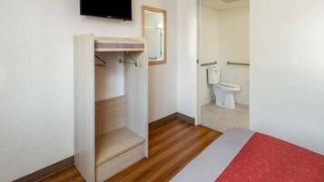 Une chambre à coucher avec un lit, un plancher en bois, une armoire, un miroir et un téléviseur.