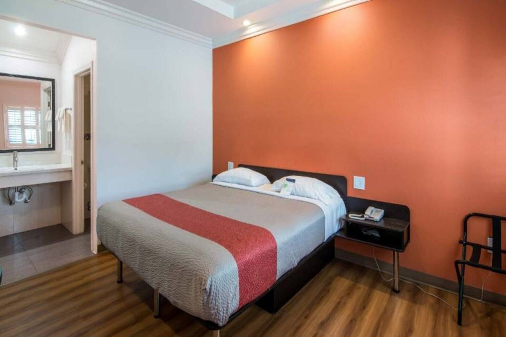 A hotel room with a bed, a nightstand, a chair, and a bathroom visible in the background.