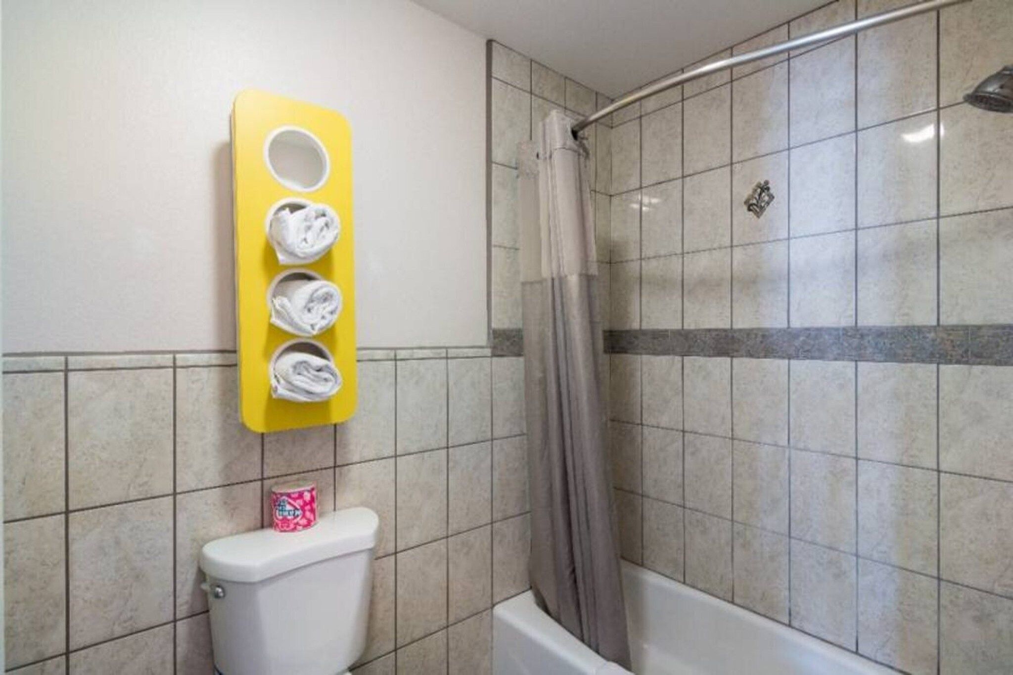 A bathroom with a toilet, a shower, and a yellow towel rack with three towels.