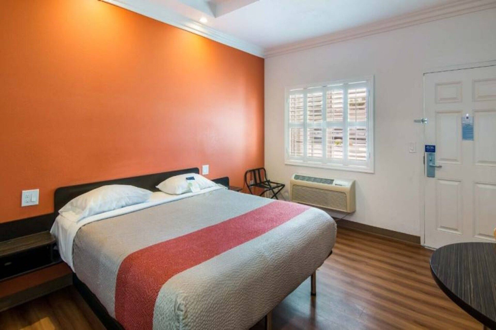 Une chambre d’hôtel équipée d’un lit, d’une chaise, d’une fenêtre avec des stores, d’une porte et d’un appareil de climatisation.