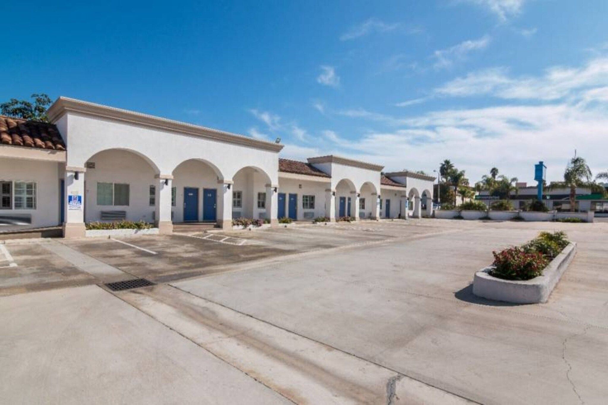A series of white buildings with arched doorways and a parking lot.