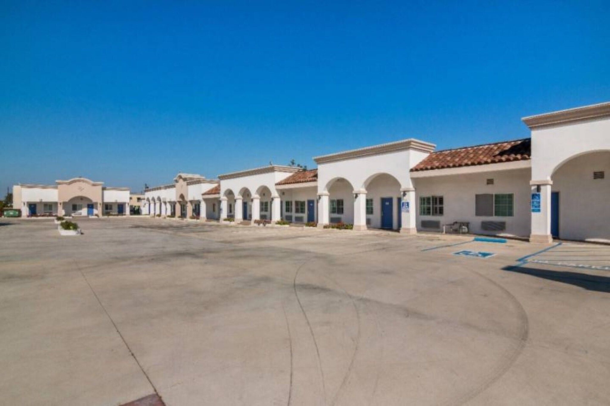 A row of white buildings with arched doorways and a clear blue sky.