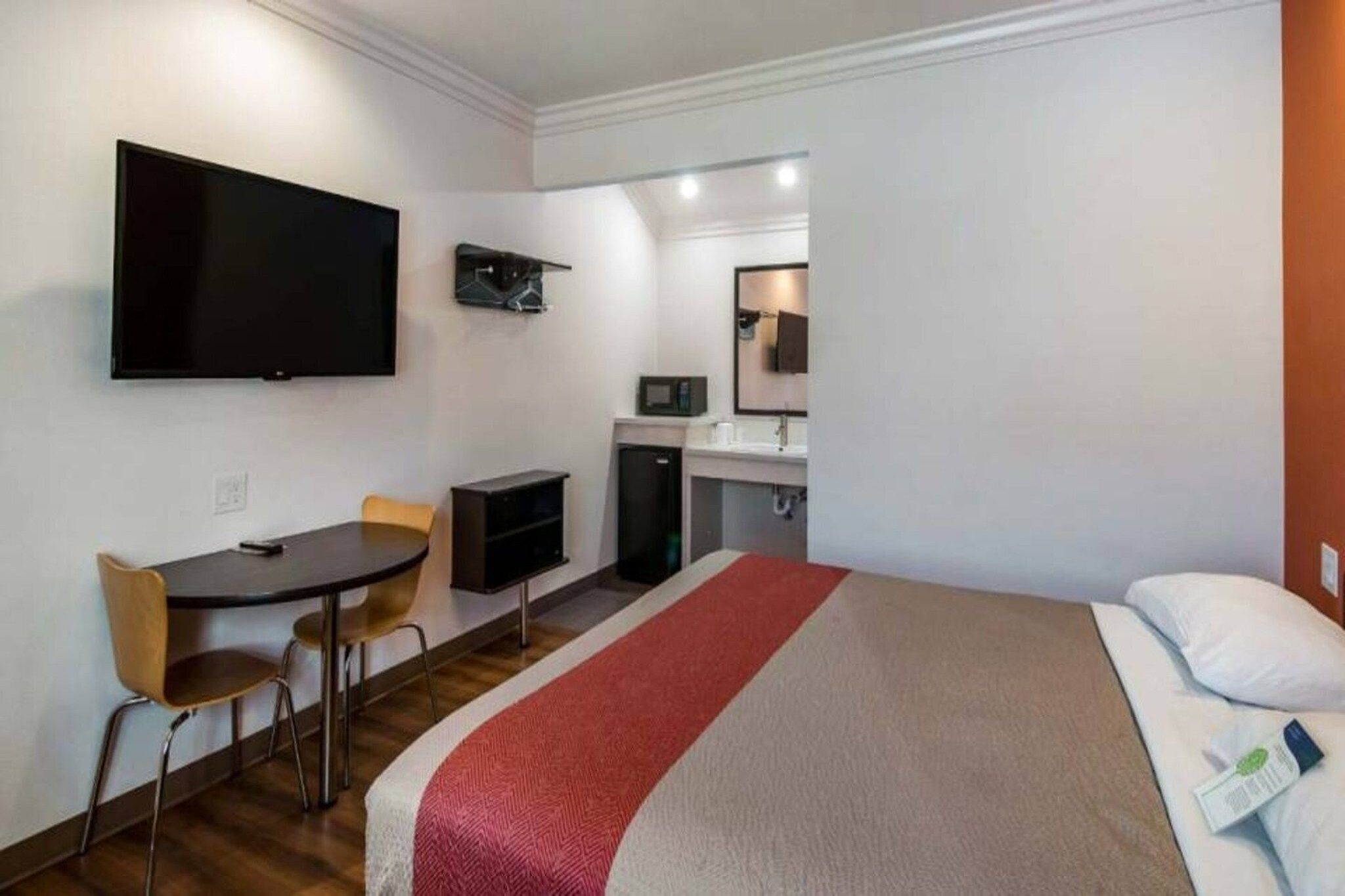 A hotel room with a bed, a desk with a chair, a television, a microwave, and a small refrigerator.
