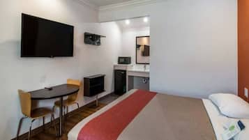 A hotel room with a bed, a desk with a chair, a television, a microwave, and a small refrigerator.