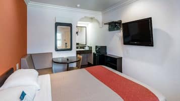A hotel room with a bed, a desk, a chair, a television, and a mirror.
