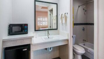 Un baño con lavamanos, espejo, inodoro, ducha y microondas.