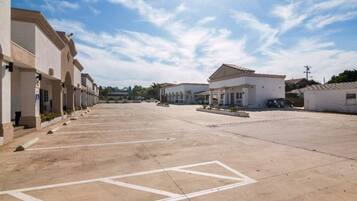 A parking lot with multiple buildings, including a large white structure with a flat roof and smaller buildings with arched windows.