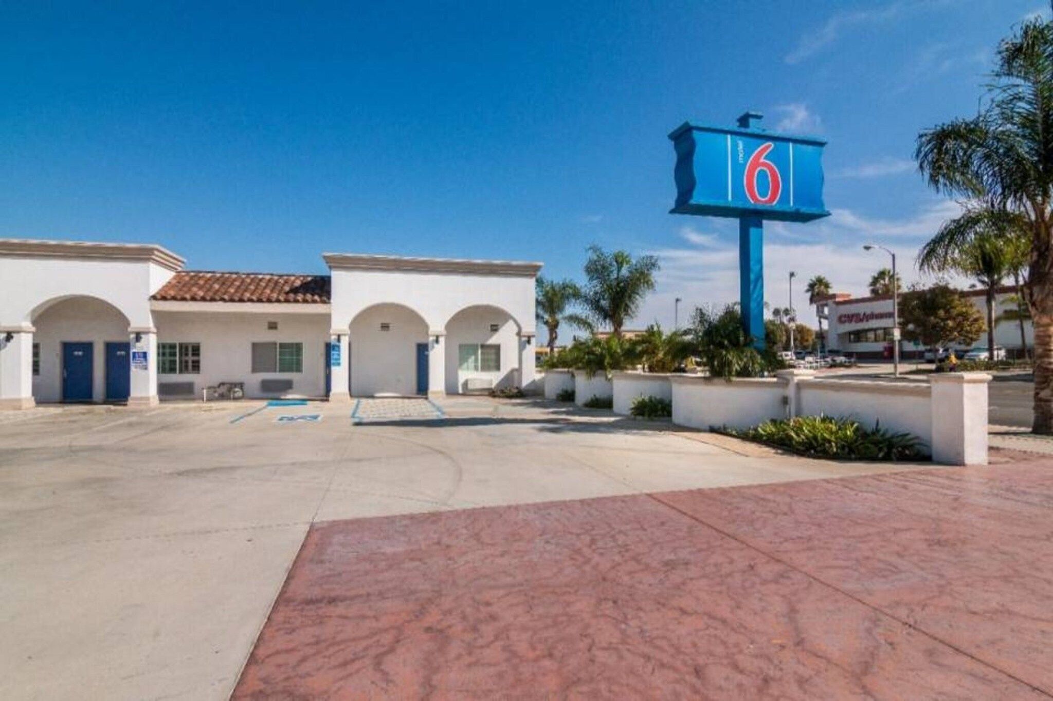 Un hôtel avec une grande enseigne bleue portant le chiffre 6, un parking et un bâtiment doté d’entrées en arc de cercle.