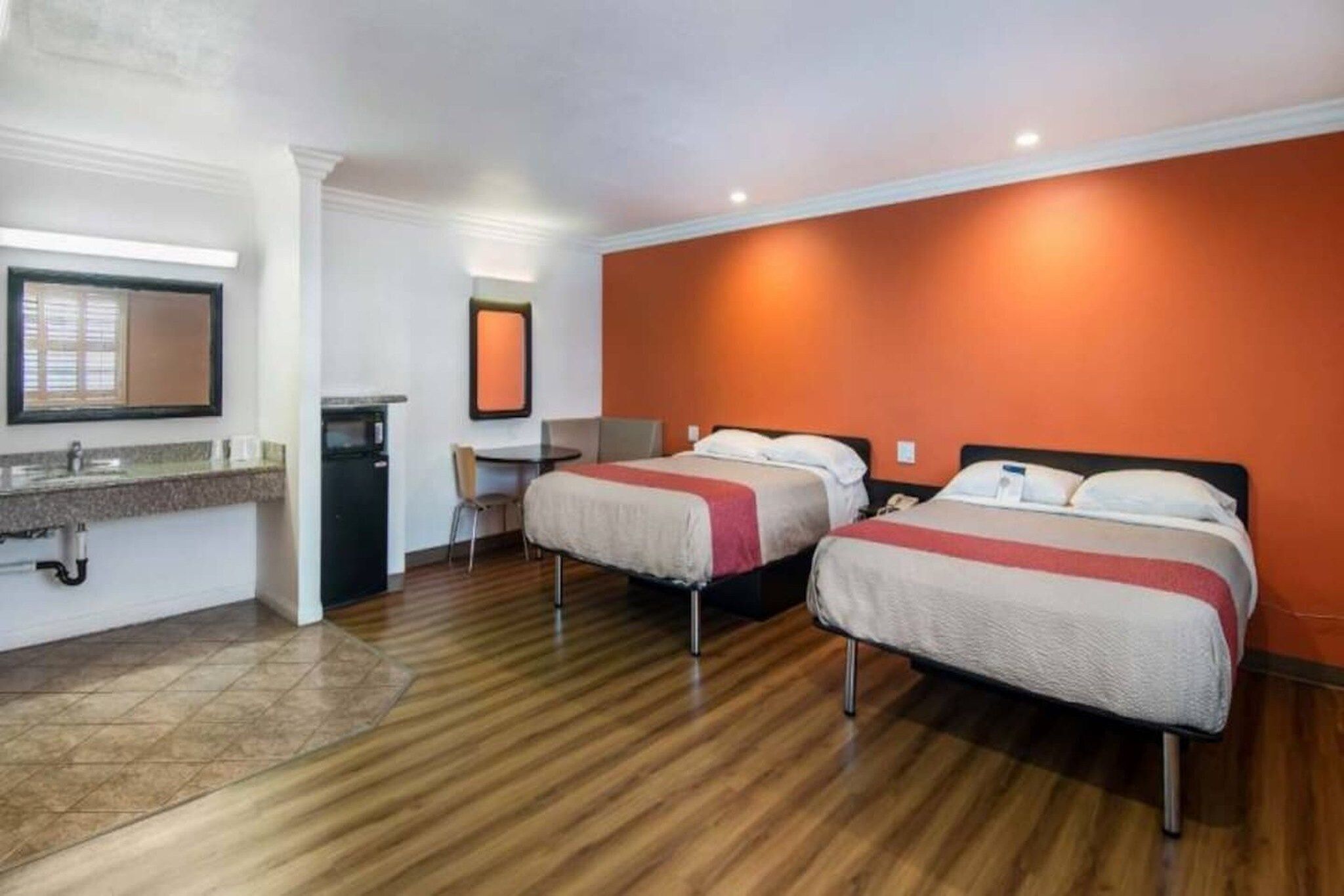Habitación de hotel con dos camas, un escritorio, una silla y una kitchenette pequeña.