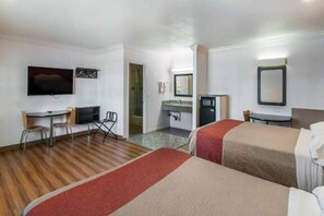 Habitación de hotel con dos camas, un escritorio, televisor, kitchenette pequeña y zona de ducha.