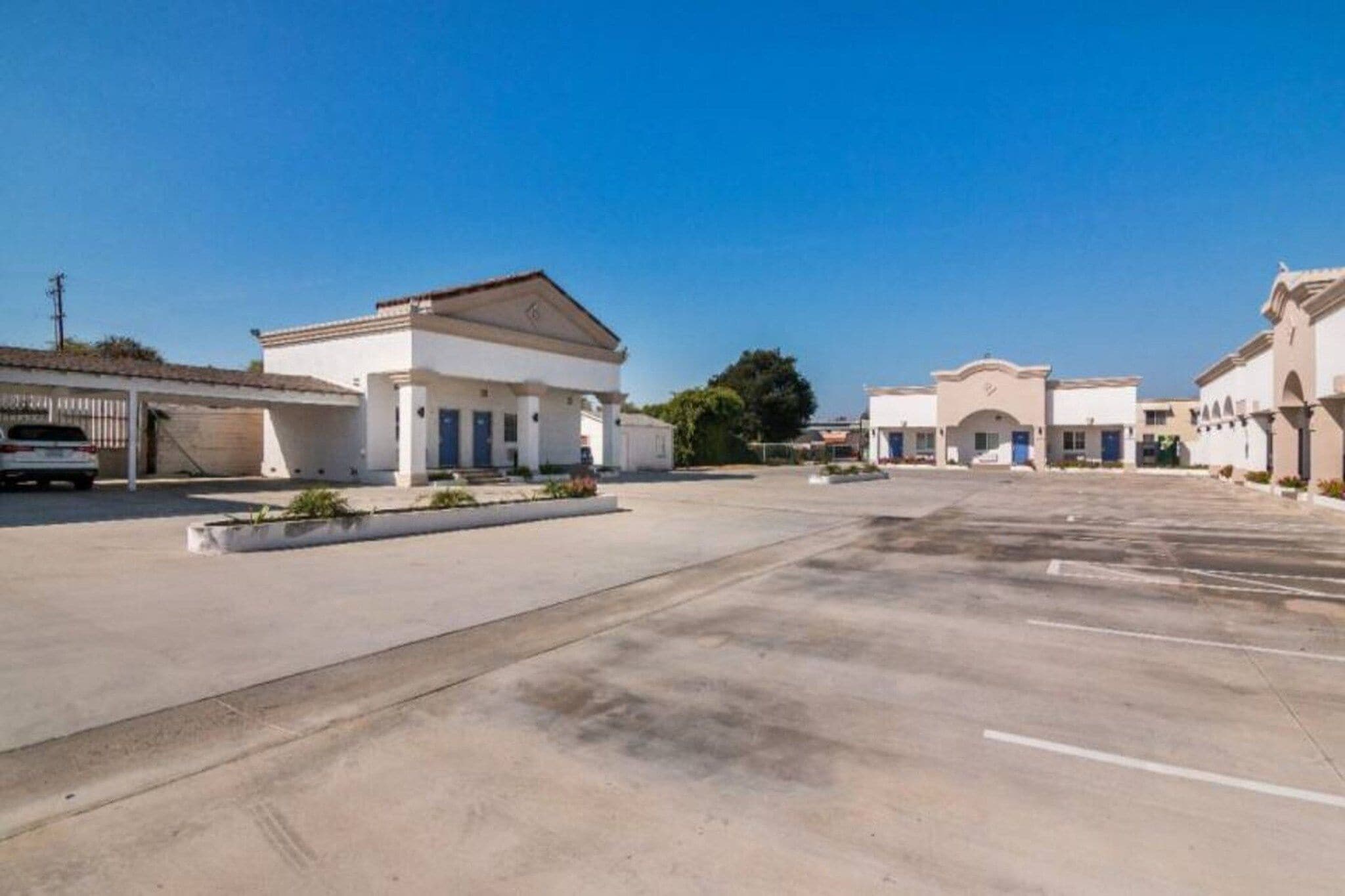 A large, empty parking lot with a row of single-story buildings, each with a flat roof and a central entrance.