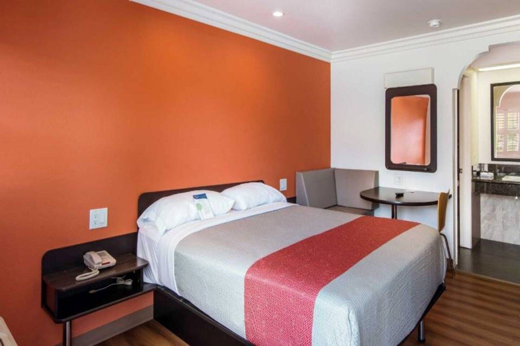 Ein Hotelzimmer mit Bett, Nachttisch, Stuhl und einem kleinen Tisch mit Spiegel.