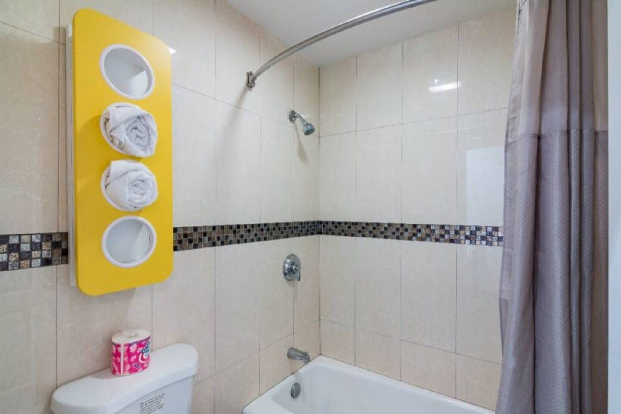 A bathroom with a shower, toilet, and a towel rack with three towels.