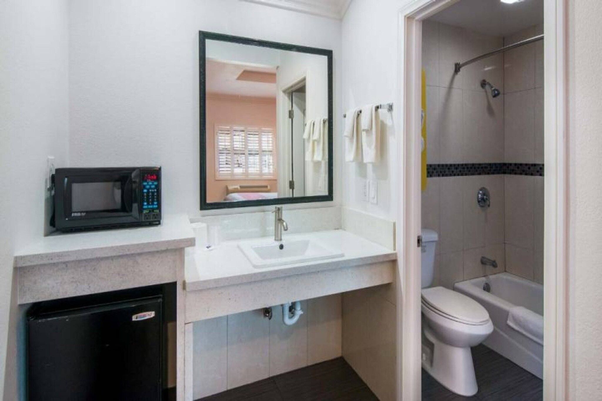 Un baño con lavamanos, espejo, inodoro, ducha y microondas.