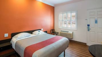 Une chambre d’hôtel équipée d’un lit, d’une chaise, d’une fenêtre avec des stores, d’une porte et d’un appareil de climatisation.
