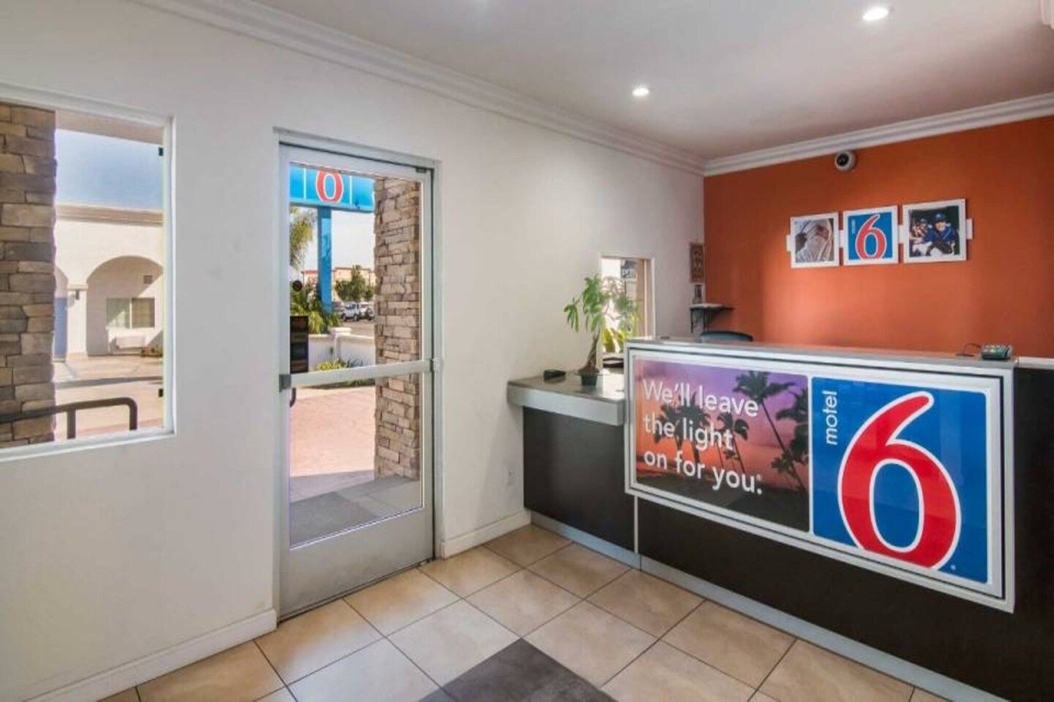 A hotel reception area with a glass door entrance, a reception desk, and a wall with a large number '6' sign.
