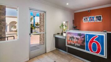 A hotel reception area with a glass door entrance, a reception desk, and a wall with a large number '6' sign.