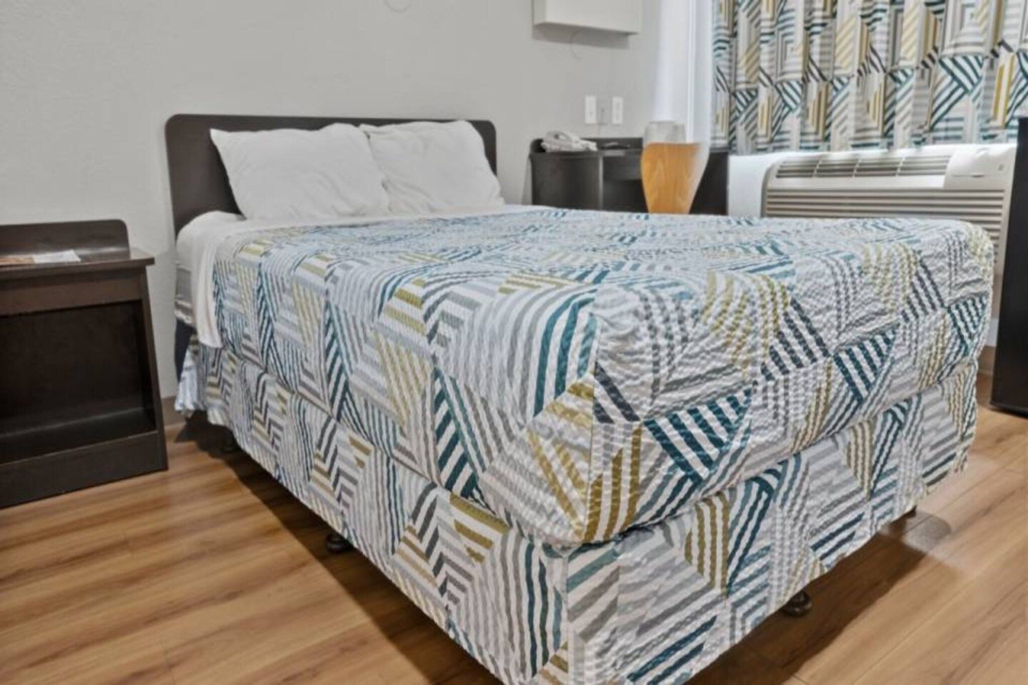 Une chambre d’hôtel avec un lit, une table de chevet, une lampe et une fenêtre avec des rideaux.