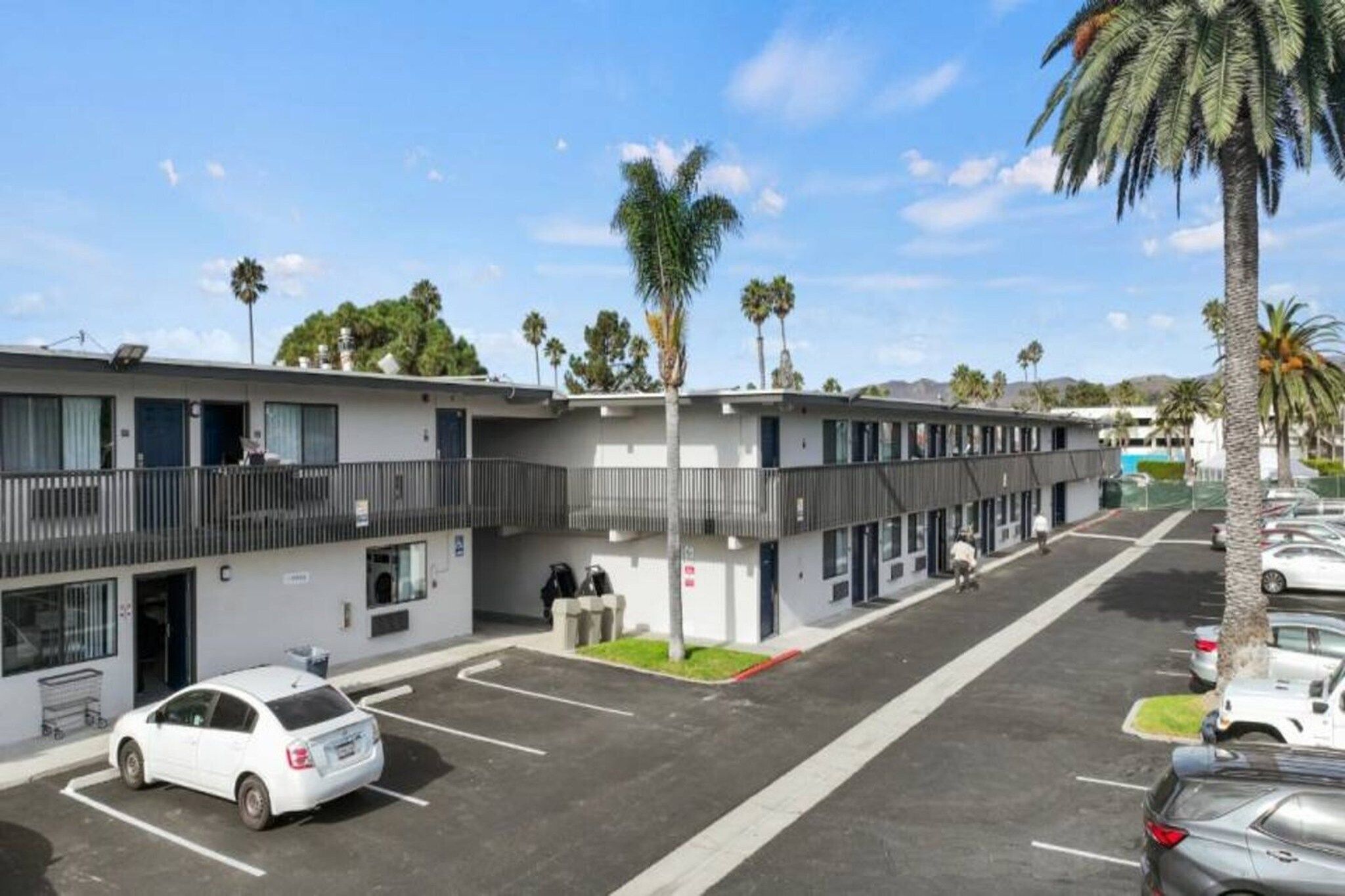 Un motel con estacionamiento, una marquesina techada y palmeras.