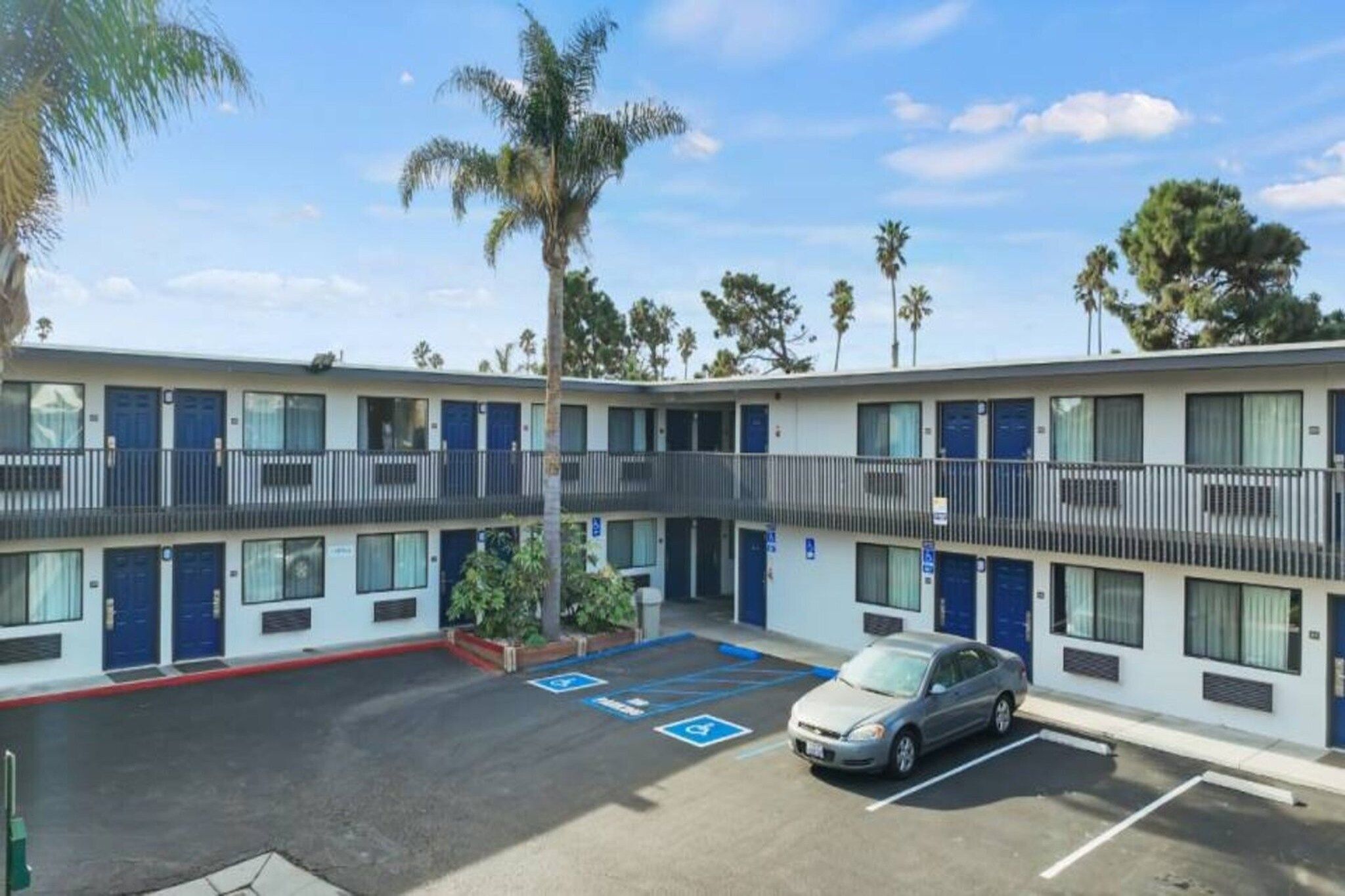A motel with a parking lot, multiple rooms, and a car parked.