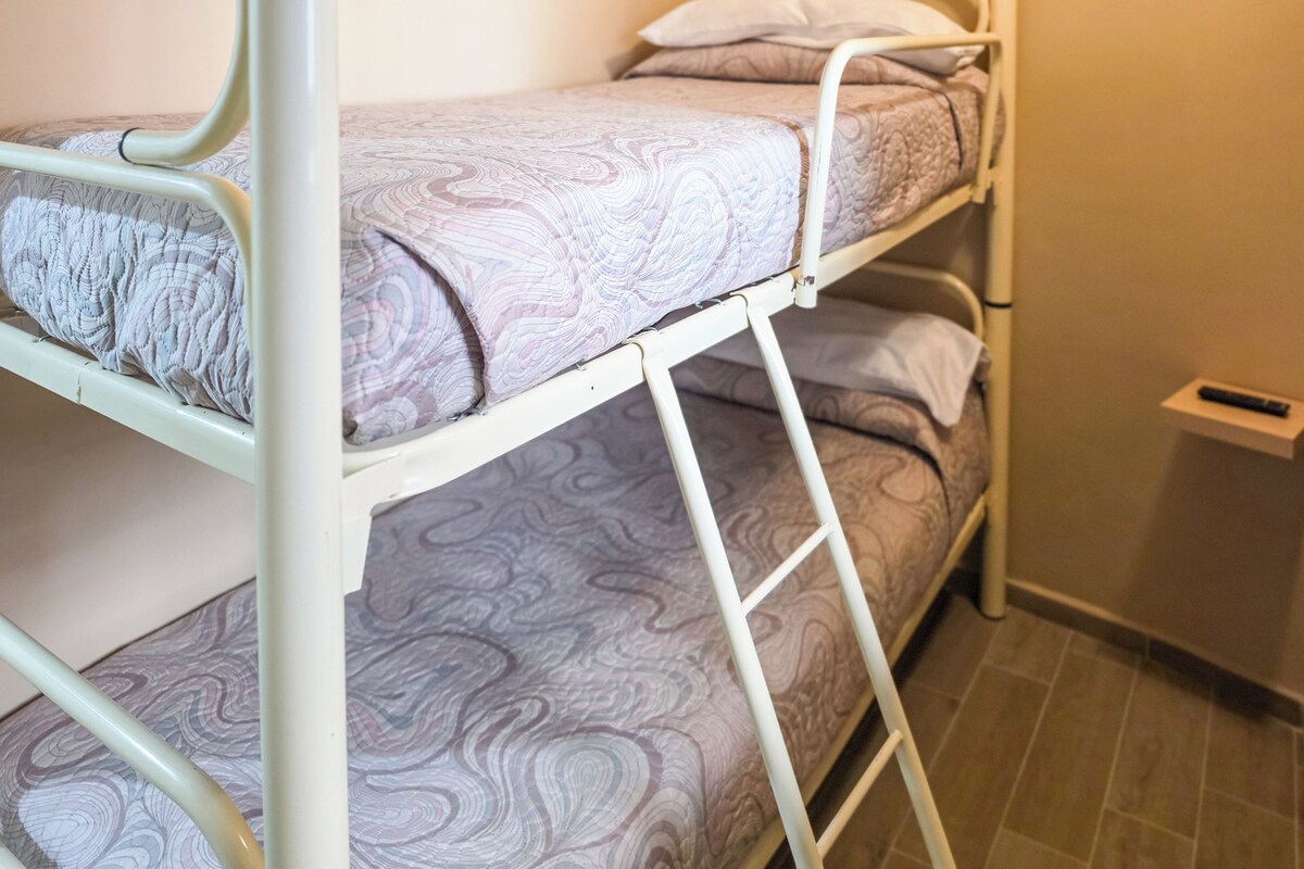 Un lit superposé avec un matelas à motifs, une structure en métal et une petite étagère à côté.