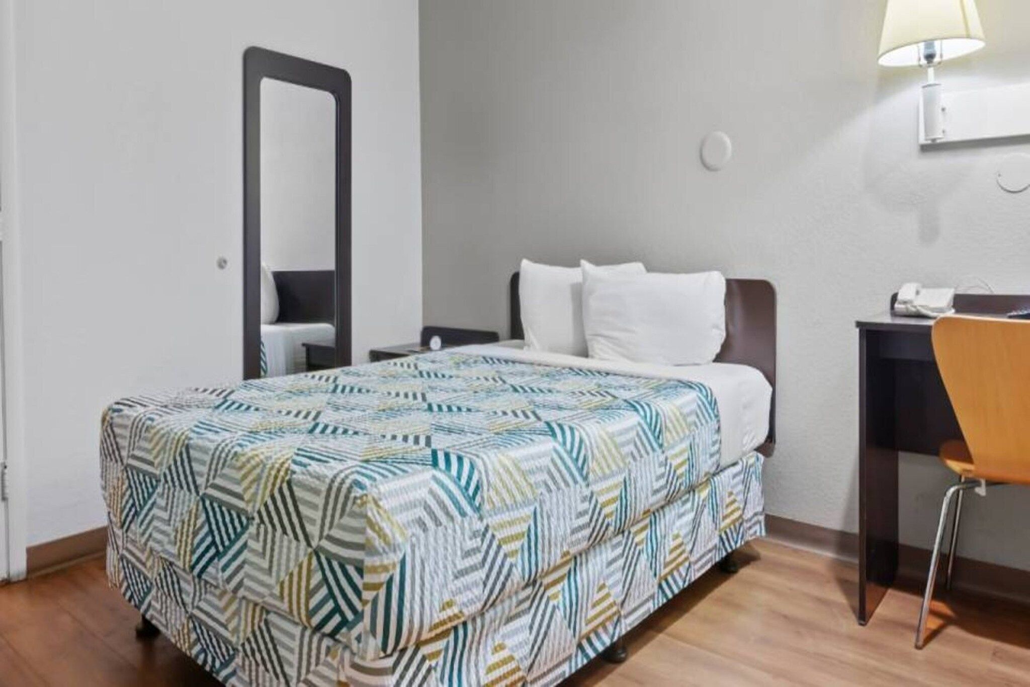 Habitación de hotel con cama, escritorio, silla, lámpara y espejo.