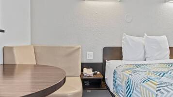 A hotel room with a bed, a small bedside table with a phone, a chair, and a round table.
