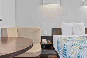 Una habitación de hotel con una cama, una mesita de noche con un teléfono, una silla y una mesa redonda.