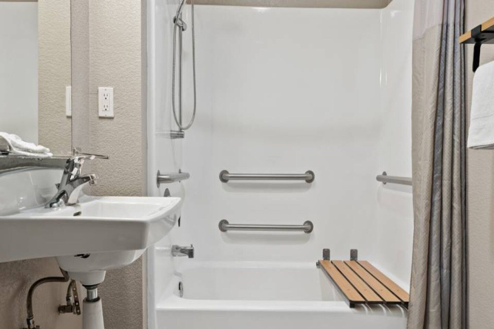 Een badkamer met een witte wastafel, een douche met glazen deur en een houten plank.