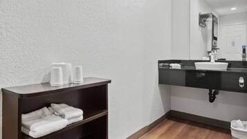 A bathroom with a dark wooden shelf holding towels, a white sink with a black countertop, and a mirror above it.