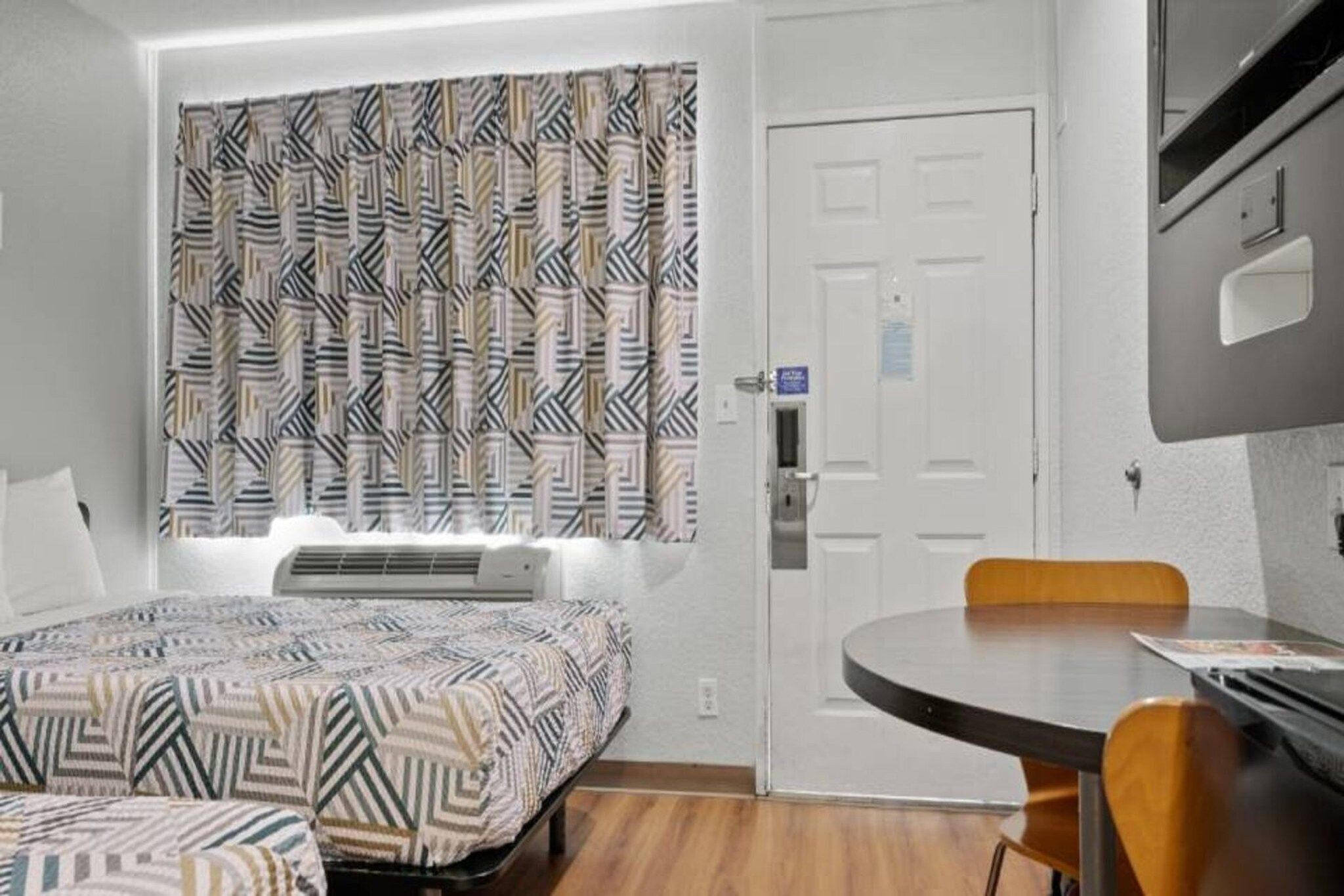 A hotel room with a bed, a desk, a chair, and a window with patterned curtains.