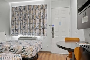 A hotel room with a bed, a desk, a chair, and a window with patterned curtains.