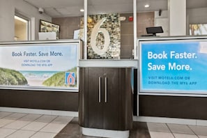 A reception area with a digital kiosk, a large number '6' on the wall, and two promotional posters encouraging visitors to book faster and save more through the My6 app. - 2 Full Beds | Mini Fridge (Ventura)