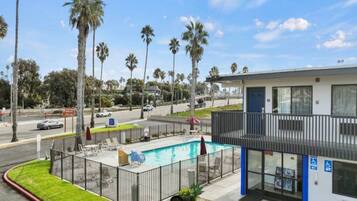 A hotel with a pool area, a fenced deck, and a parking lot with palm trees.