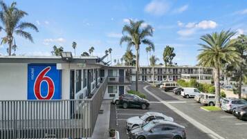A motel with a prominent number sign, a parking lot with cars, and palm trees in the background.