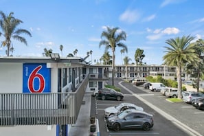 A motel with a prominent number sign, a parking lot with cars, and palm trees in the background. - 2 Full Beds | Mini Fridge (Ventura)