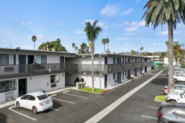 A motel with a parking lot, a covered walkway, and palm trees.