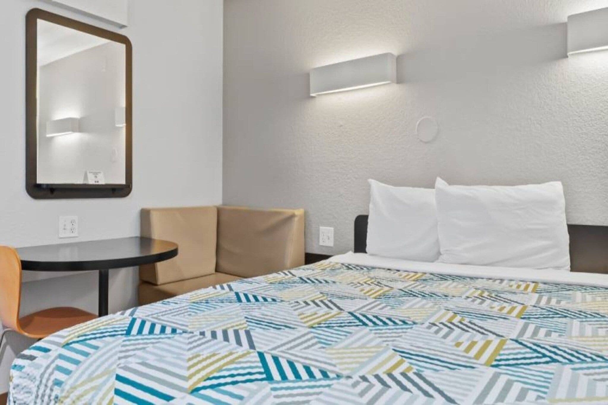 A hotel room with a bed, a chair, a small table, and a mirror.