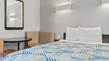 A hotel room with a bed, a chair, a small table, and a mirror.