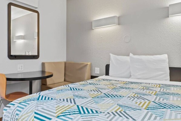 A hotel room with a bed, a chair, a small table, and a mirror. - 1 Full Bed | ADA/RI Shower/Mini Fridge (Ventura)