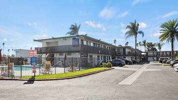 A multi-story hotel with a pool area, parking lot, and palm trees.