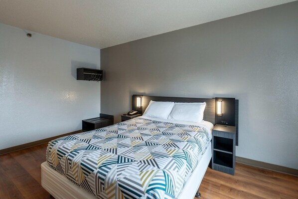 A modern hotel room with a large bed, a bedside table, a wall-mounted TV, and a nightstand.