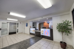A hotel reception area with a reception desk, a clock, and a potted plant.