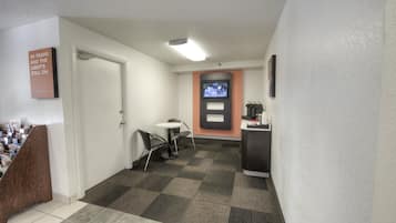 A hotel lobby with a reception desk, a television mounted on the wall, and a door leading to a room.
